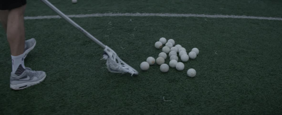 A person picks up a lacrosse ball with his stick
