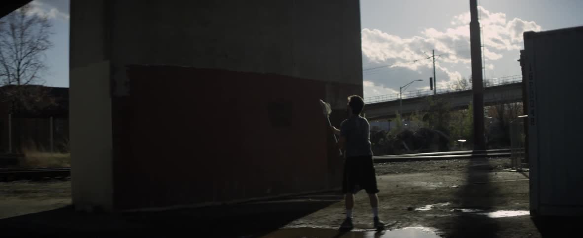 A man is tossing a ball at a wall with a lacrosse stick