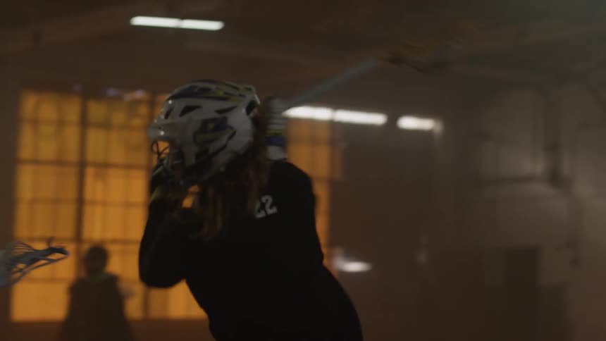 Group of people play lacrosse in a dim warehouse