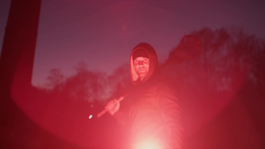 A man is holding a lacrosse stick and lit flare at night