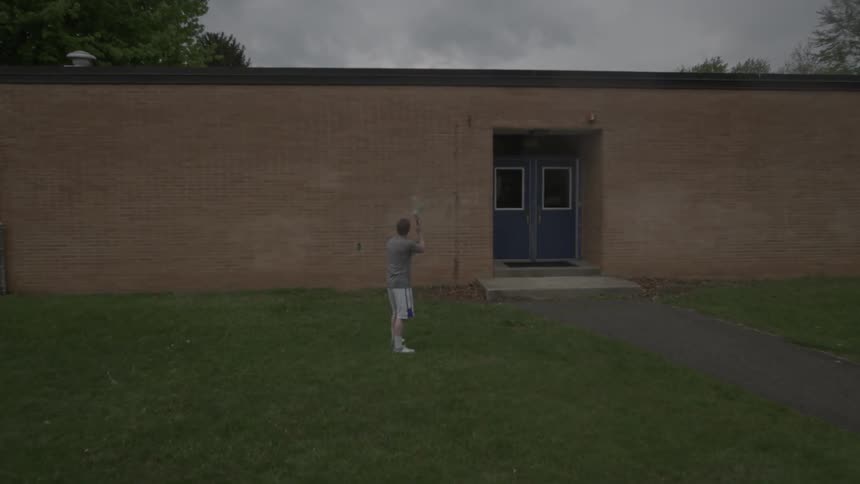 Man uses lacrosse stick to throw a ball at a brick building