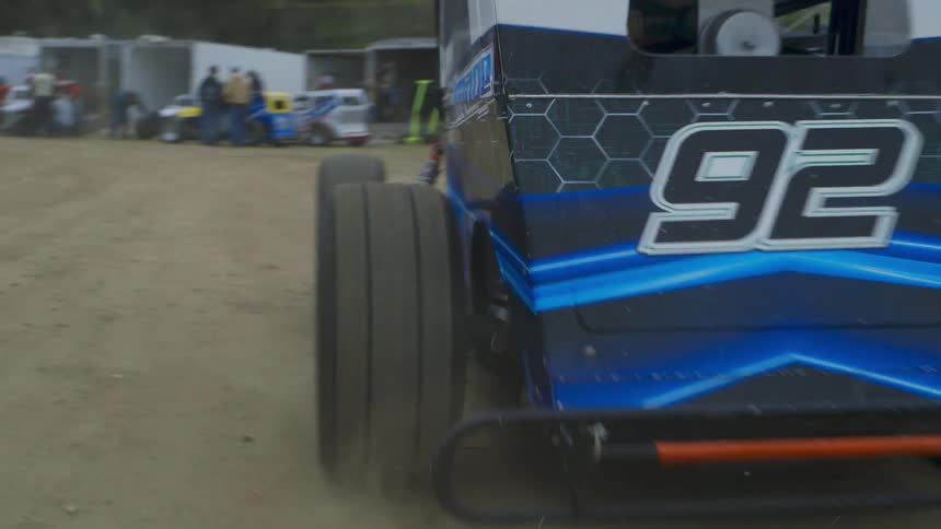 A car rides down the dirt road past a crowd
