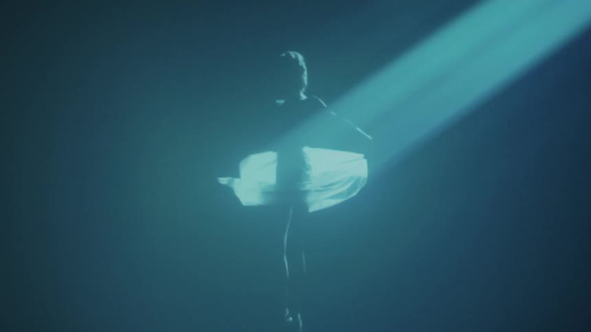 A woman in a white dress dances under a spotlight