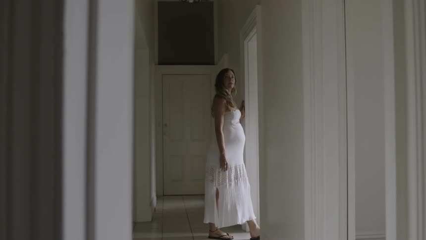 Pregnant woman in a white dress walks through a doorway