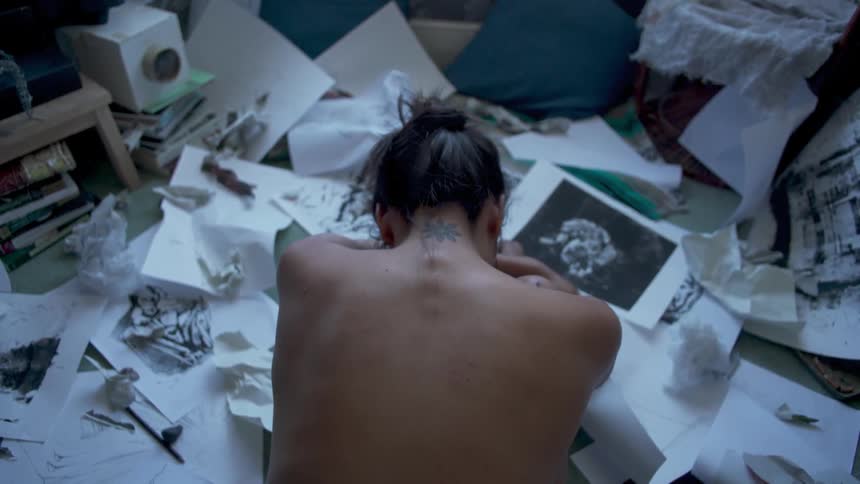 Shirtless person leaning forward in a mess of papers spread out on the floor