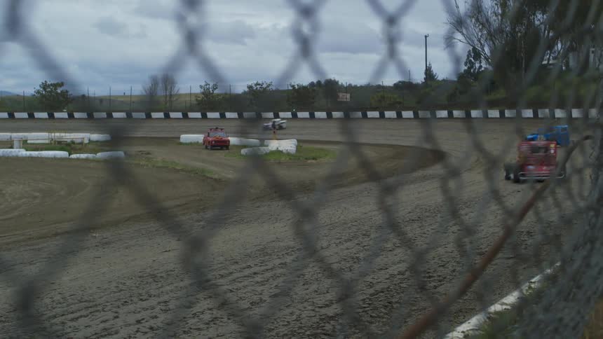 Cars race fast around the dirt turn on the track
