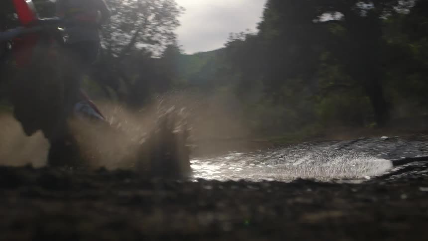 A man rides a dirt bike through a puddle