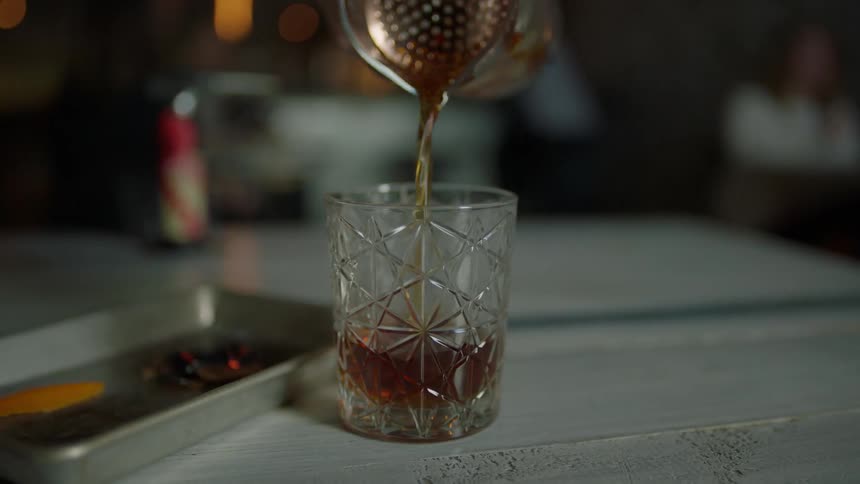 A person pours a drink in a small glass