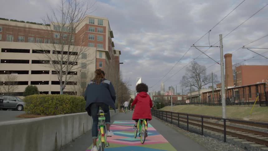 Two women ride bicycles on the sidewalk