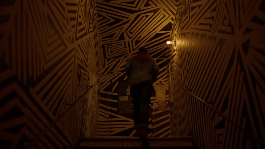 A person jogs up a dimly lit stairwell with a black and white design all over the walls