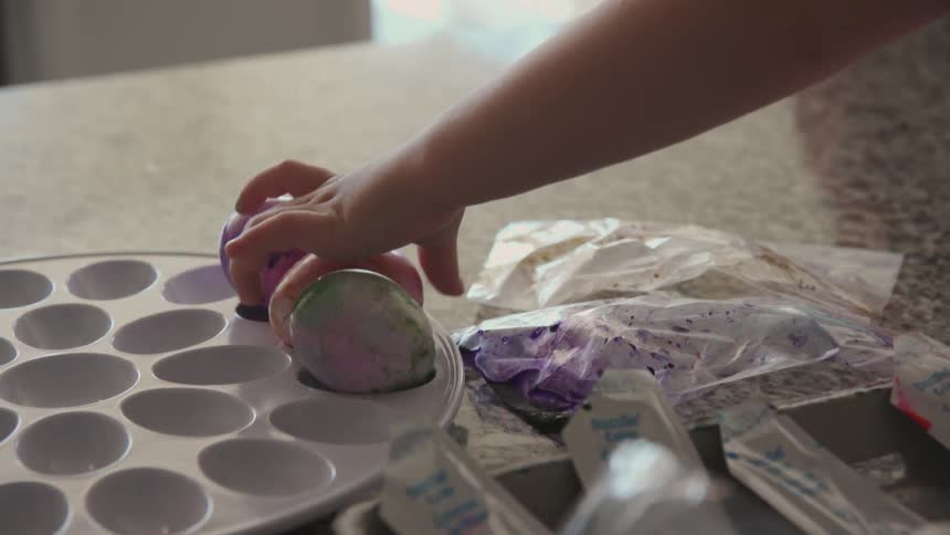 A child is placing dyed eggs in a tray