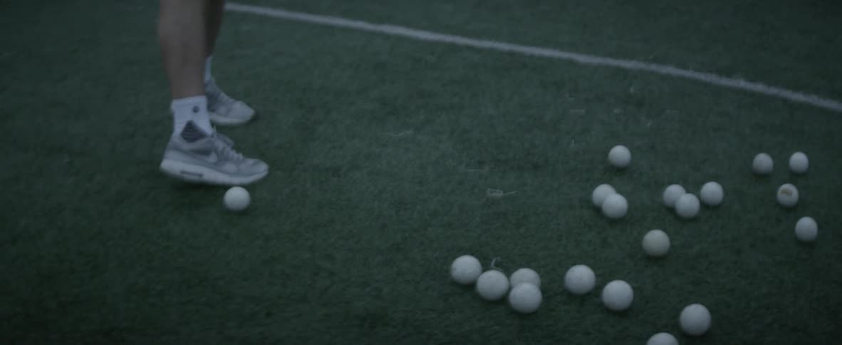 A man picks up a ball with a lacrosse stick