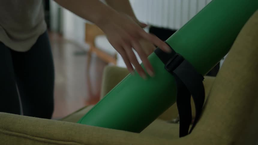 A woman grabs a green yoga mat off a chair