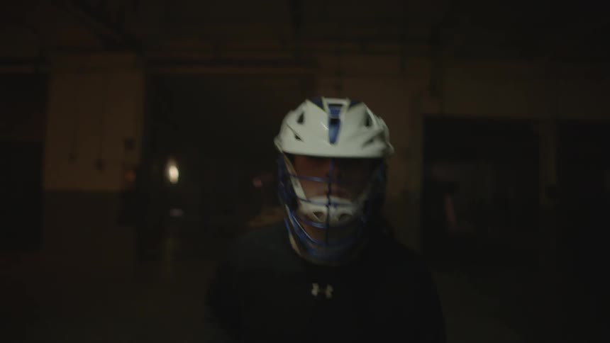 A man plays lacrosse in a dark warehouse