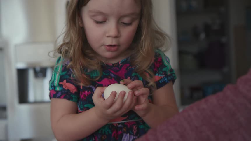 A little girl is holding onto an egg as she sits on a kitchen counter