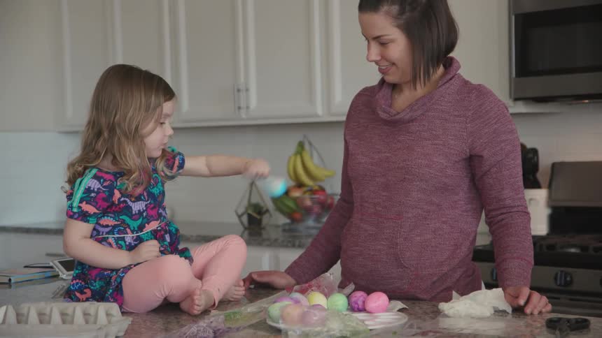 A woman helps a young girl dye eggs