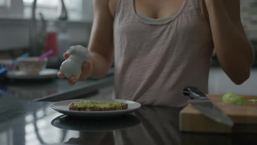 A woman sprinkles salt on avocado toast