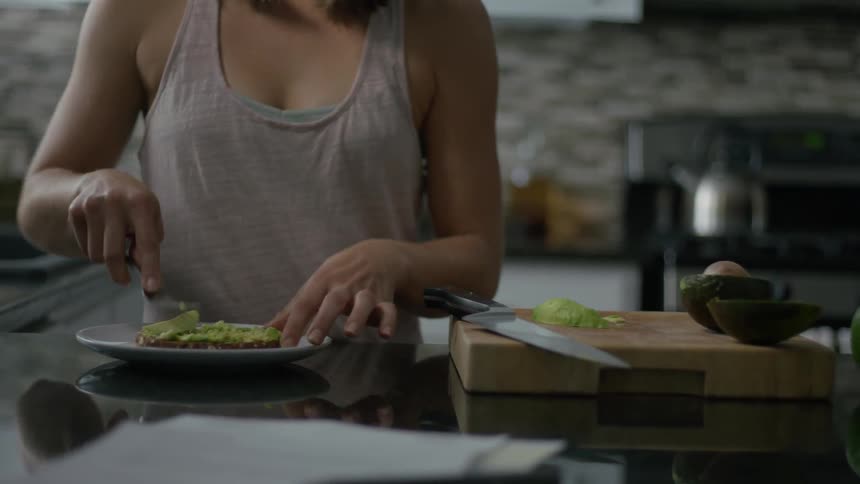 A woman is putting food on bread in the kitchen