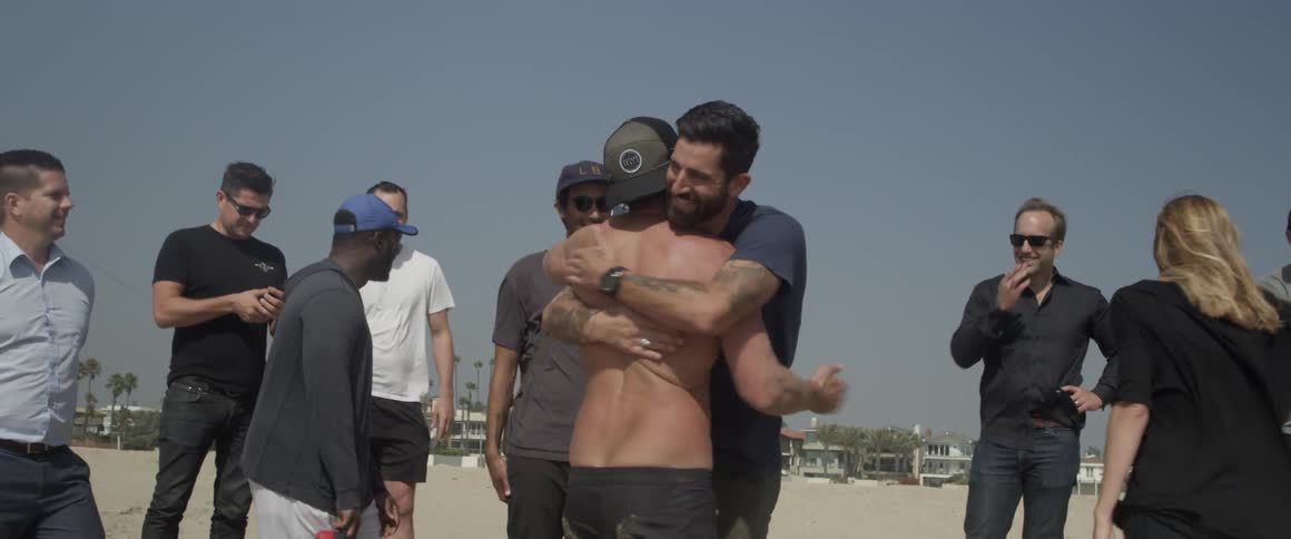 Two men in a group at the beach hug each other