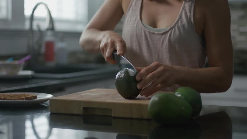 Woman in kitchen cutting avocado in half