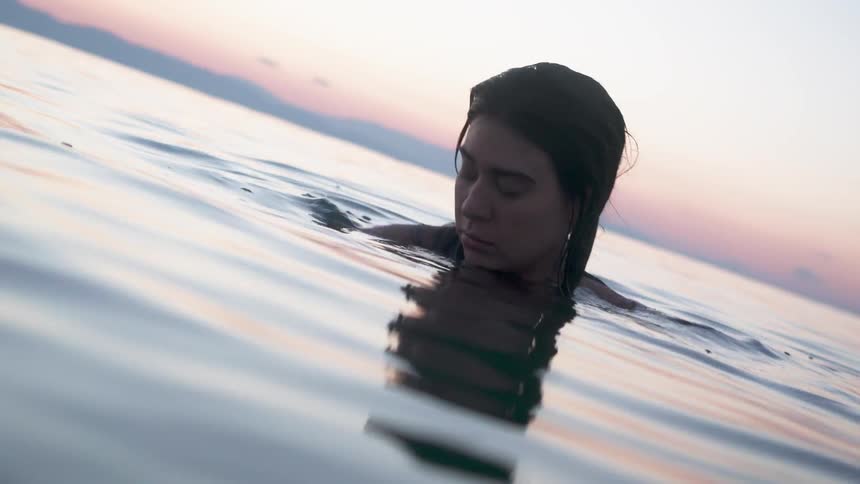 A woman looks scared while swimming in a lake at sunset
