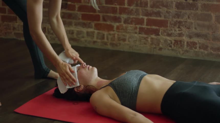 A woman places a rag on the forehead of a woman doing yoga