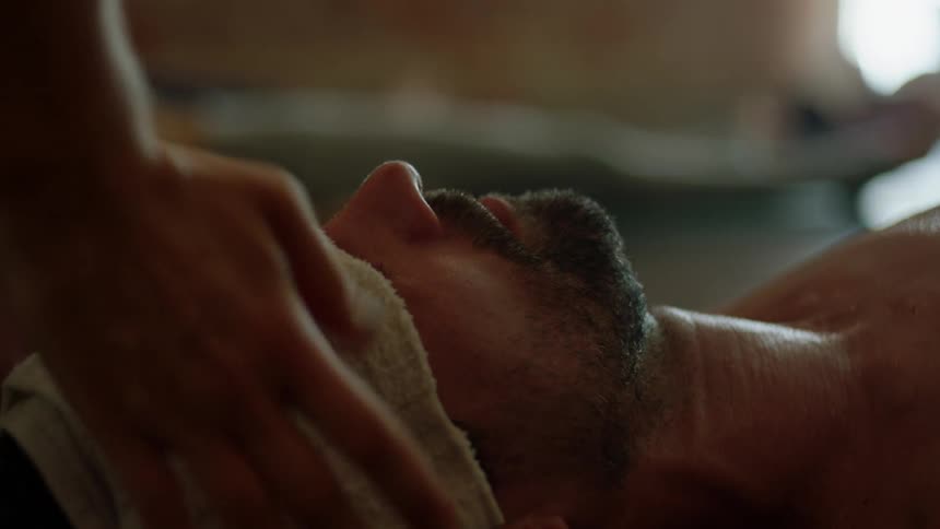 A person presses down then removes a wet cloth from a man's forehead