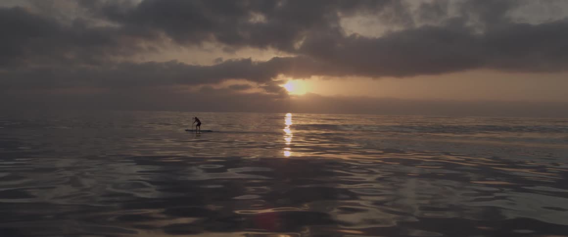 Person paddles in the middle of a large body of water while standing on a raft