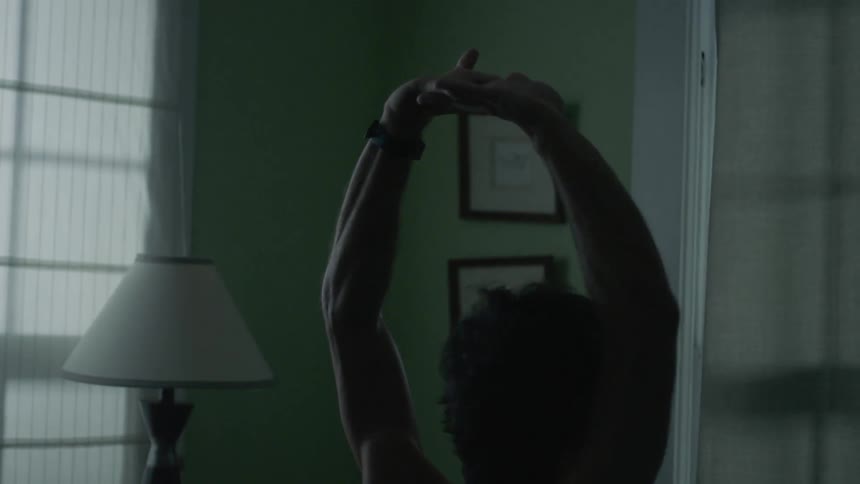 A man sits on a bed and stretches his arms
