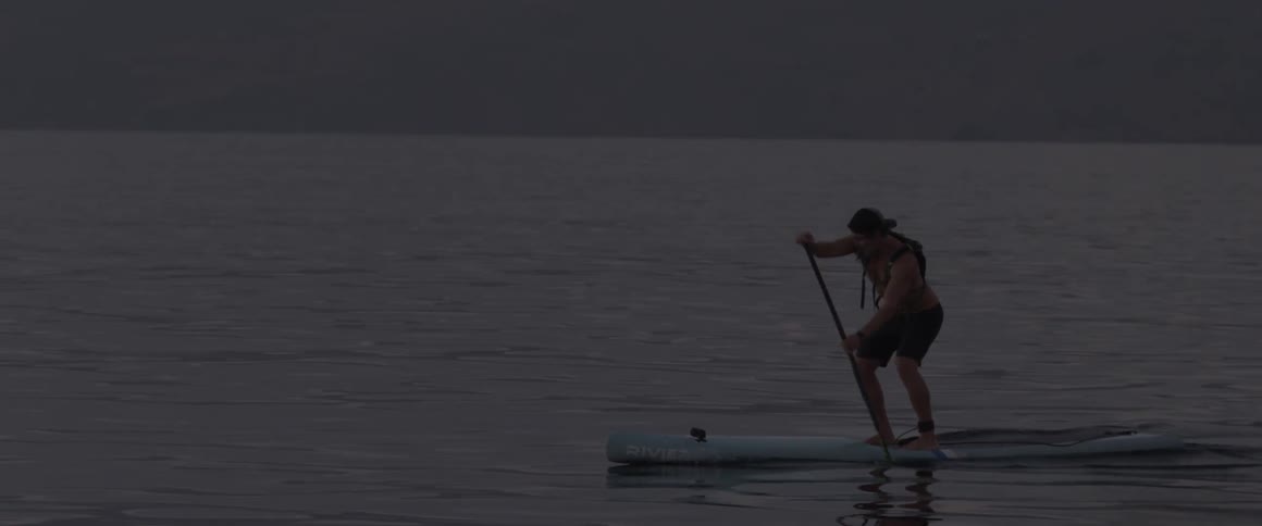 A man paddles while standing on a surfboard