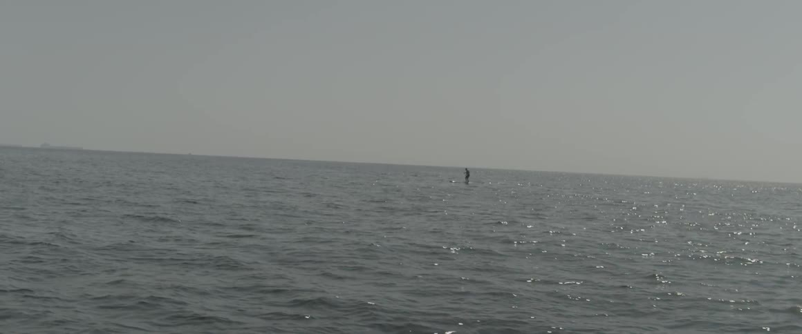 A person is floating on a surfboard in the distance