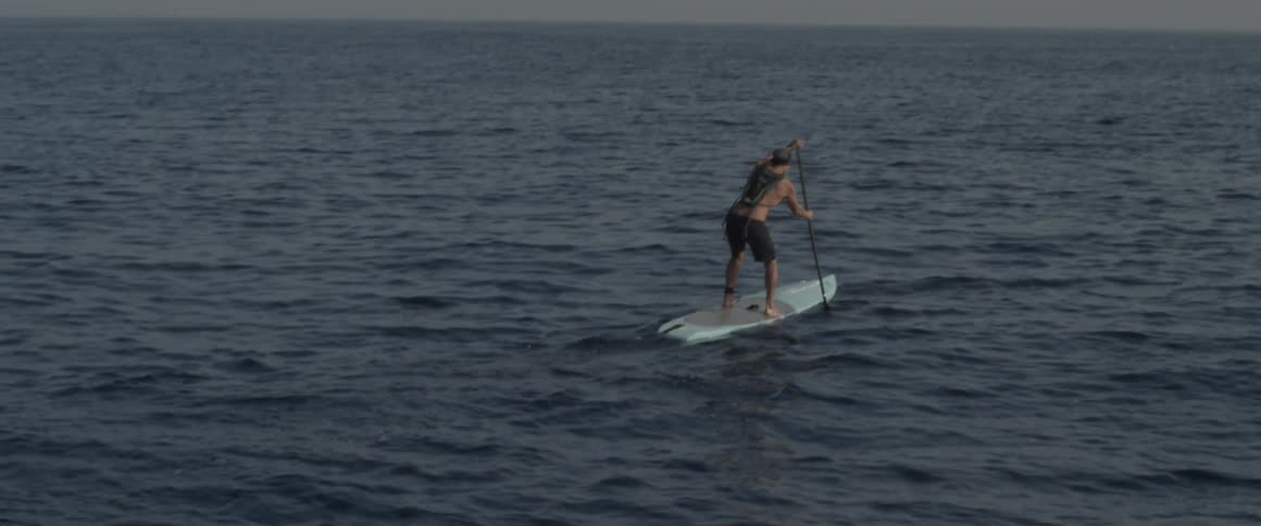 A man is on a large board paddling on a cloudy day