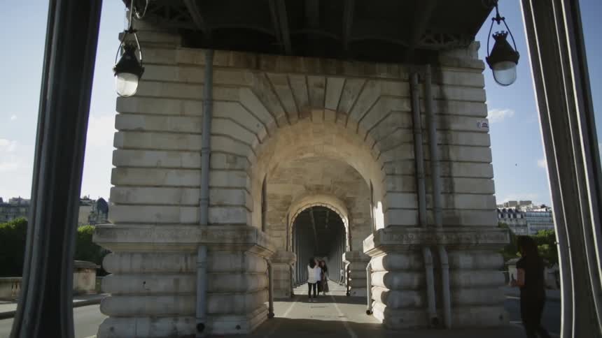 People walk under a stone pathway