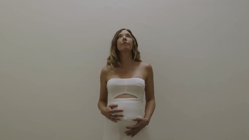 A pregnant woman rubs her belly in a white room