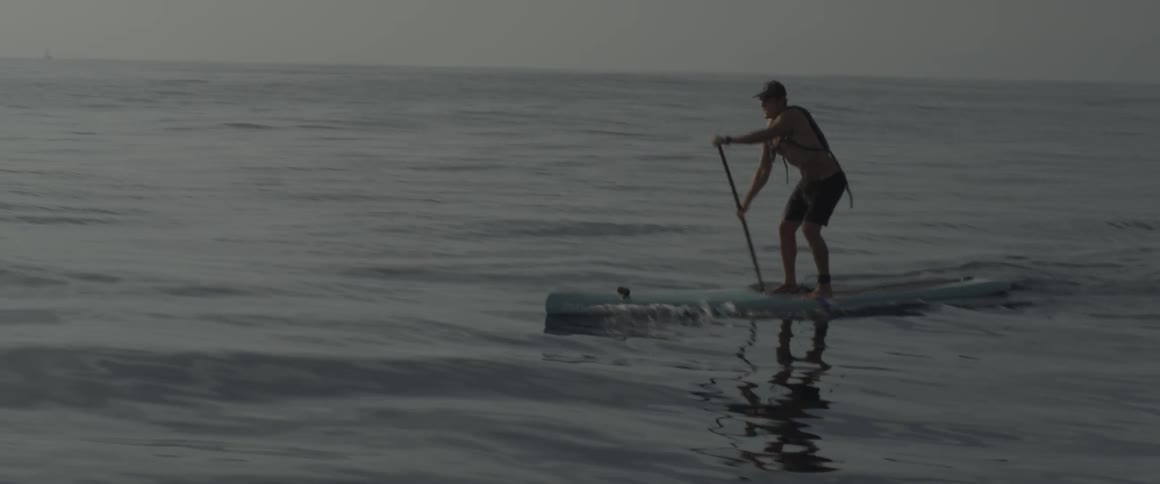 Man standing on a surfboard rows with a paddle