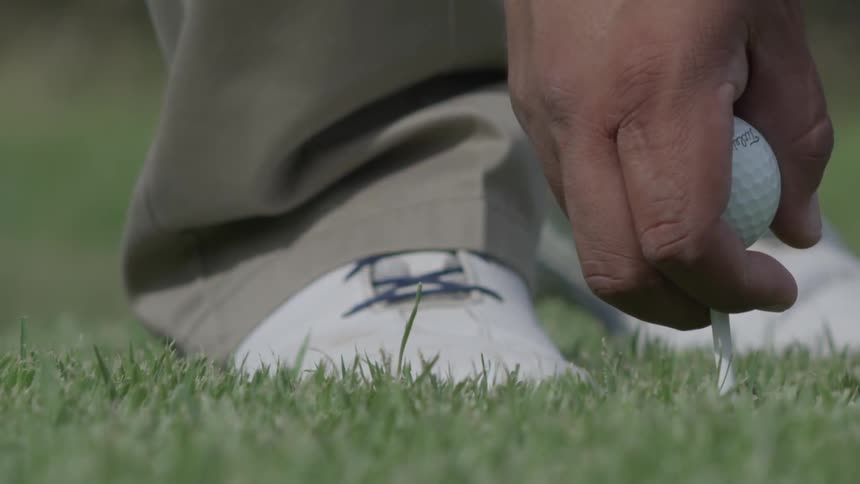A man is placing a golf ball and tee