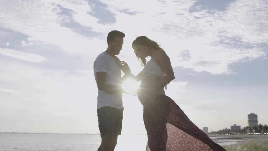 A man and pregnant woman stand next to a lake on a sunny day