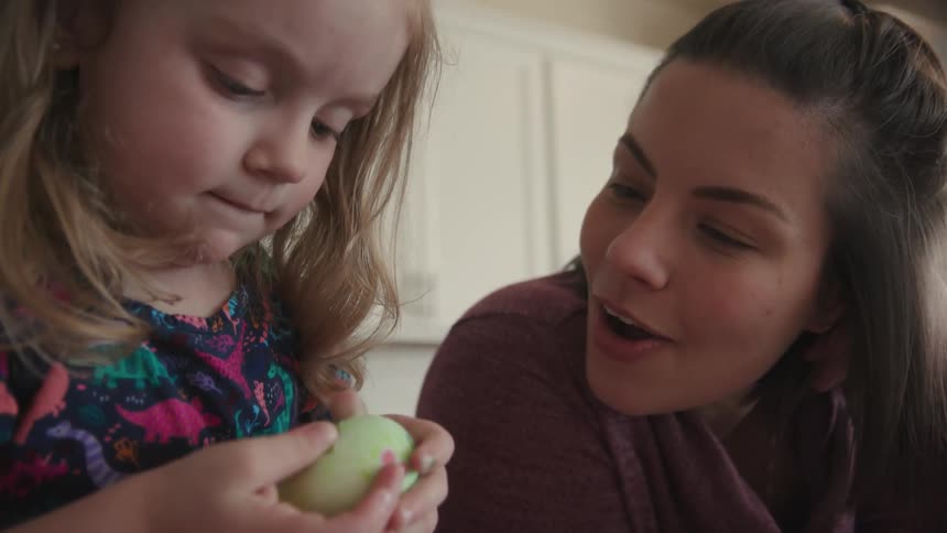 A woman smiles at a girl holding a dyed egg