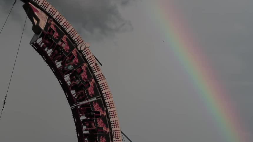 A rainbow is in the sky over a roller coaster loop