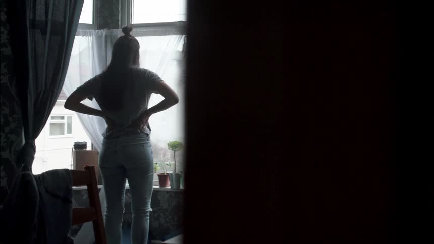 A woman walks to look out of her window