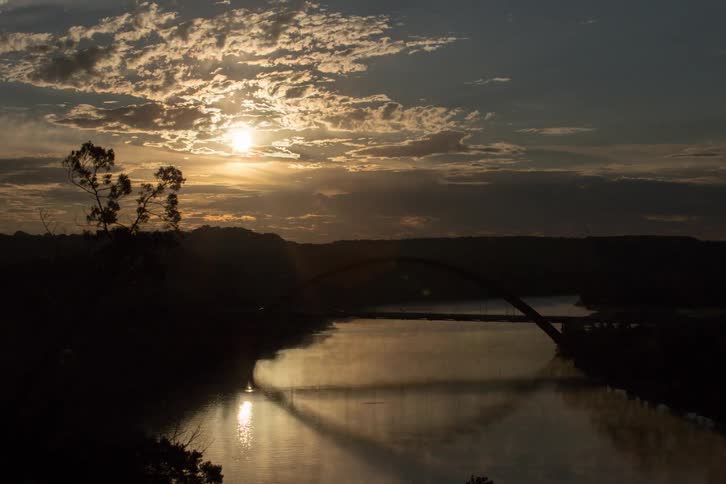 Cars drive over a river bridge as the sun rises