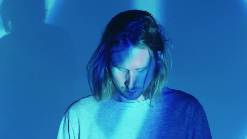 A man stands in front of blue lights that prism on the wall