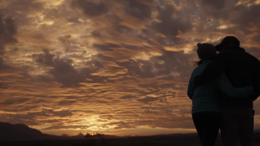 A man and woman cuddle while watching a mountain sunset