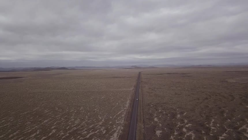 A vehicle passes down a road between open land