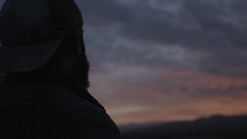 A man looks up at the cloudy dawn sky