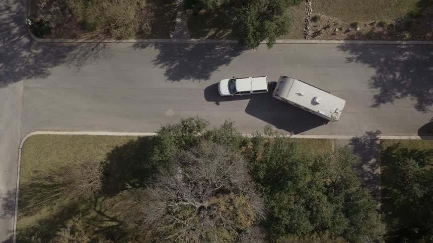 Car with attached camper pulling out of driveway and driving away