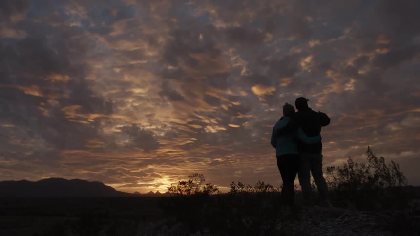 A man and woman embrace as the sun sets