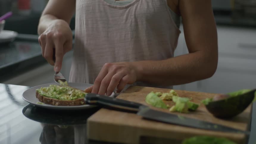 Woman spreading avocado on a slice of bread in a kitchen