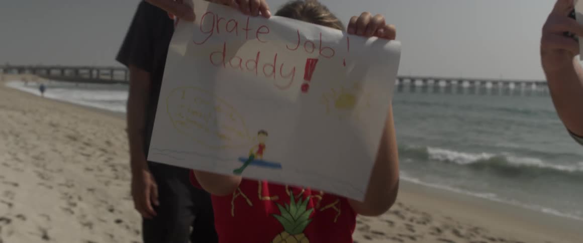 A young child holds up a handmade sign on the beach