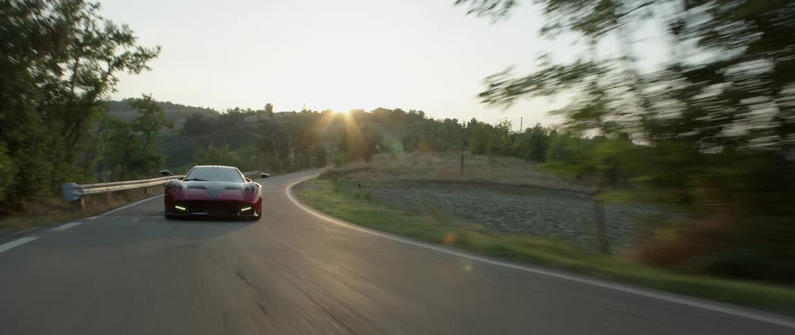 A sports car drives on a rural road at sunset
